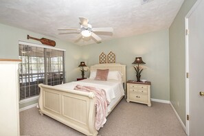 A bedroom with a bed, nightstands, a ceiling fan, a window with blinds, and a door.