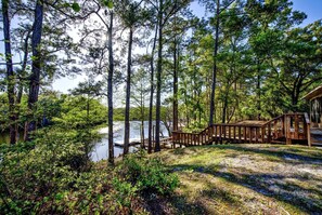 A wooden deck leading to a cabin by a lake surrounded by tall trees.