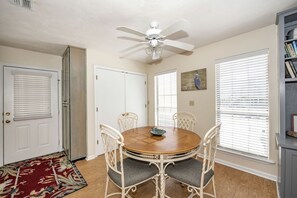 A dining room with a round wooden table, white chairs, a ceiling fan, and a bookshelf.