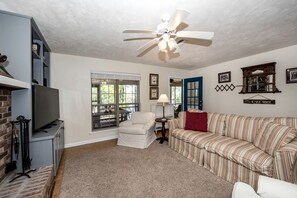 A living room with a TV, a ceiling fan, a striped sofa, a chair, and a bookshelf.