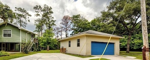 Une maison à deux étages avec un garage bleu, entourée d’arbres et sous un ciel dégagé.