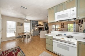 A kitchen with a stove, microwave, and cabinets. There is a dining table with chairs and a ceiling fan.