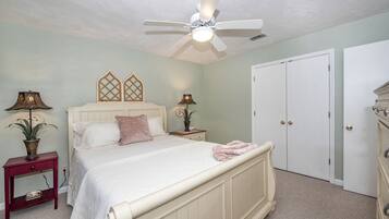 Une chambre à coucher comprenant un lit, deux tables de chevet, un ventilateur de plafond, une armoire et une porte.