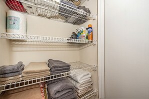 A storage closet with shelves holding towels, cleaning supplies, and a rolled-up item. - Cabin Getaway: Pet-Friendly Oasis on the Ochlockonee River Bend, Ideal for Fishing and Swimming (Wakulla County)