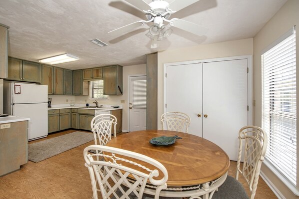 A kitchen with a dining table, chairs, a ceiling fan, and a refrigerator. - Cabin Getaway: Pet-Friendly Oasis on the Ochlockonee River Bend, Ideal for Fishing and Swimming (Wakulla County)