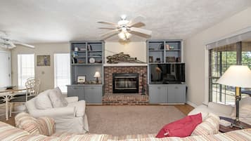 A living room with a fireplace, a ceiling fan, and a TV.