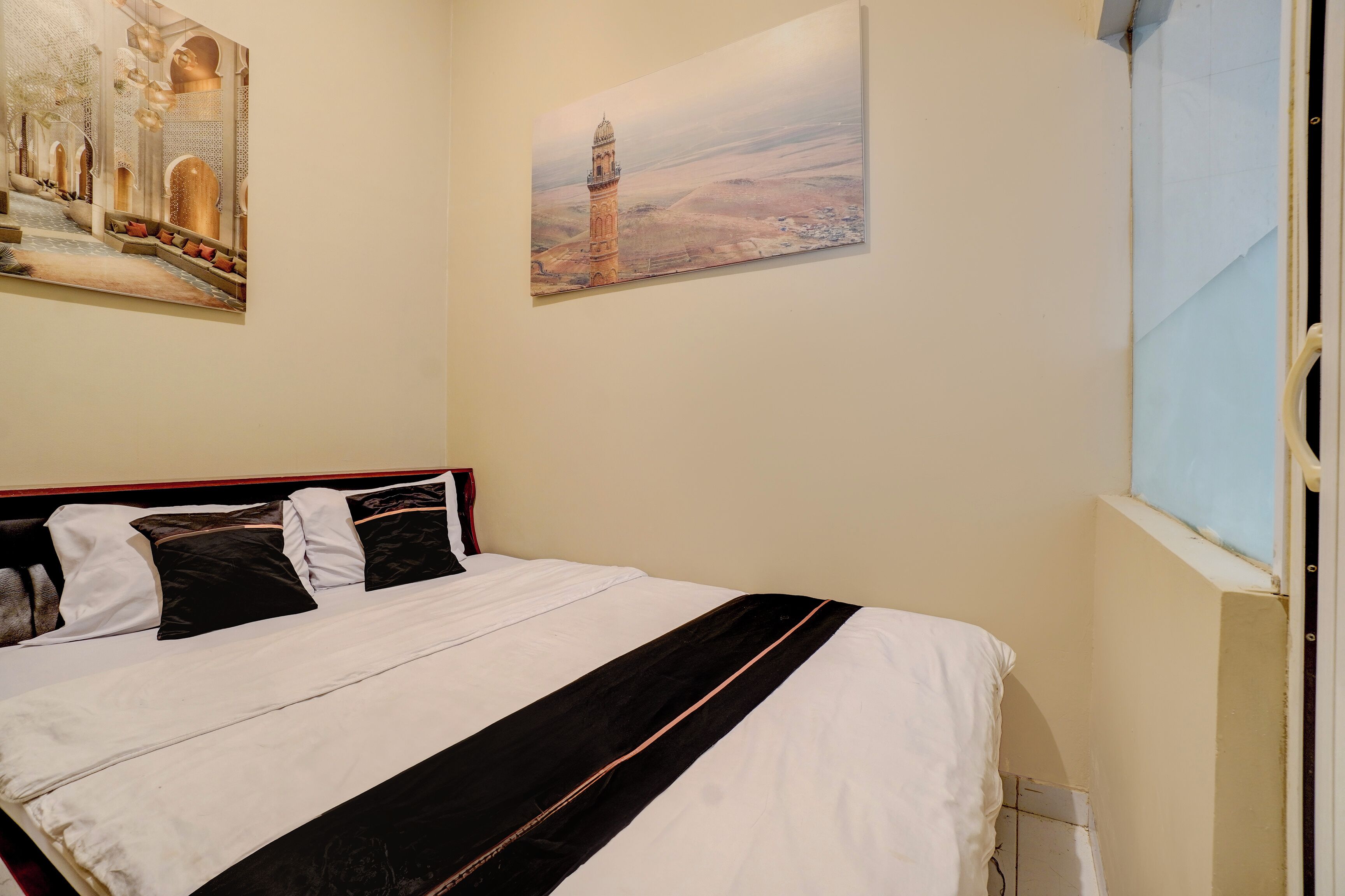A hotel room with a bed, a window, and two paintings on the wall.