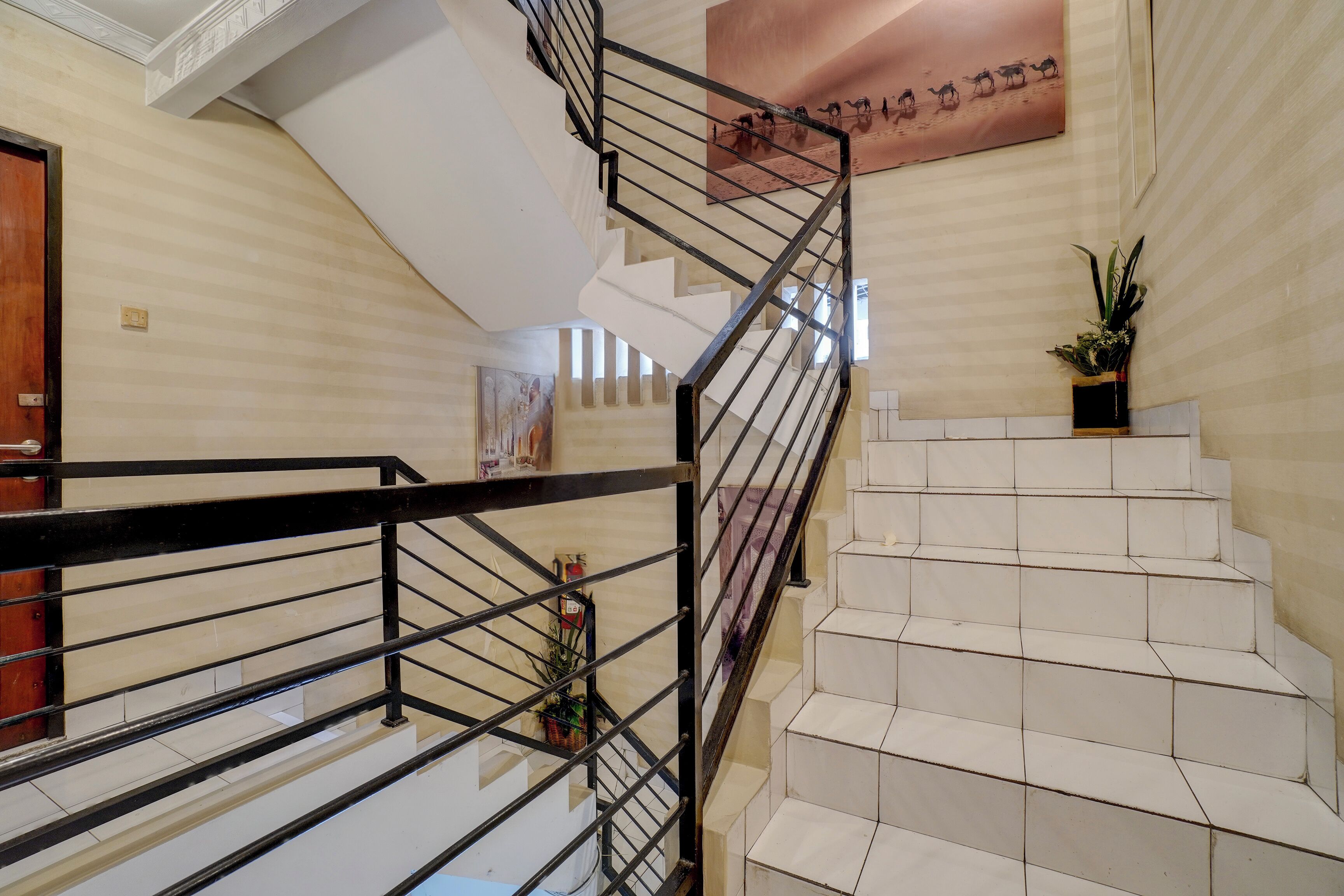 A modern staircase with a black metal railing, white steps, and a potted plant on the landing.