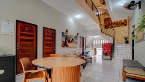 Amplia sala de estar con una mesa redonda de madera, dos sillas de mimbre, un sofá y una escalera que sube a un nivel superior.