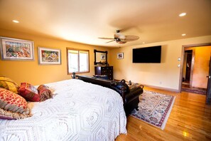 A bedroom with a large bed, a ceiling fan, a TV, and a door leading to another room. - Luxury Cottage Ranch with Hot-Tub, Theater and Pool Table in Watauga County, North Carolina (Sugar Grove)