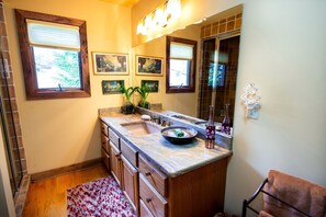 A bathroom with a marble countertop, wooden cabinets, a sink, a mirror, and framed artwork on the wall. - Luxury Cottage Ranch with Hot-Tub, Theater and Pool Table in Watauga County, North Carolina (Sugar Grove)