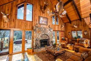 A rustic interior with a stone fireplace, leather furniture, and deer antlers as decor. - Luxury Cottage Ranch with Hot-Tub, Theater and Pool Table in Watauga County, North Carolina (Sugar Grove)