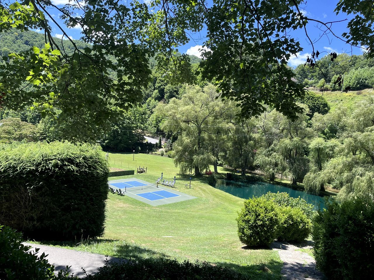 A tennis court surrounded by lush greenery and a small pond.