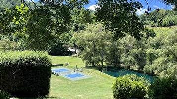 A tennis court surrounded by lush greenery and a small pond.