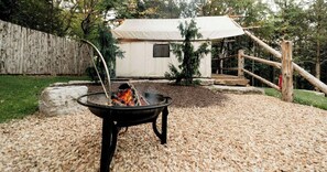 A tent with a fire pit in a wooded backyard.