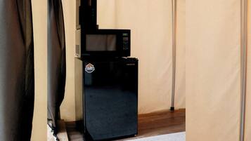A black refrigerator with a microwave on top, placed in a corner of a room with beige walls and a wooden floor.