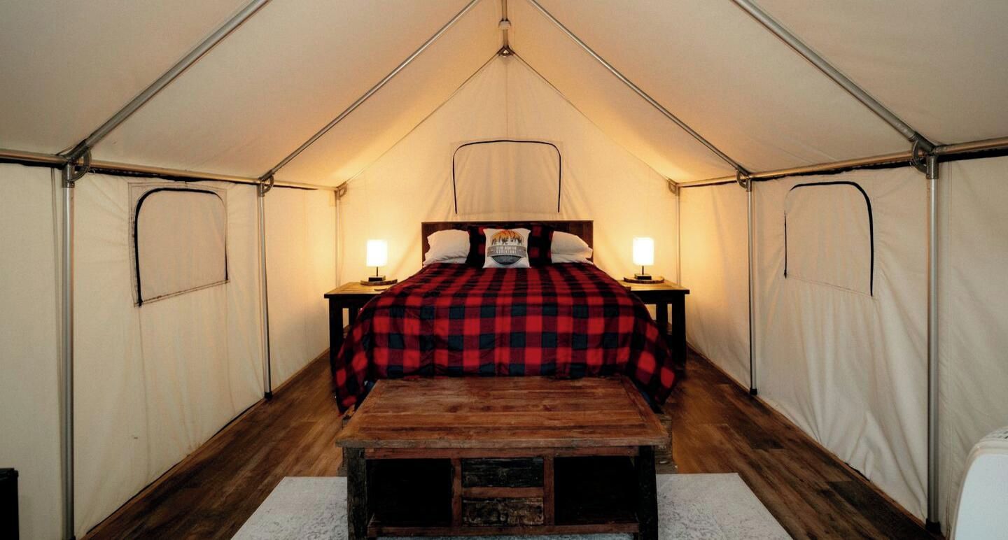A tent with a bed, two bedside lamps, and a wooden bench.