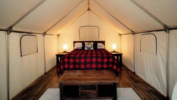 A tent with a bed, two bedside lamps, and a wooden bench.