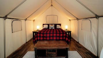 A tent with a bed, two bedside lamps, and a wooden bench.
