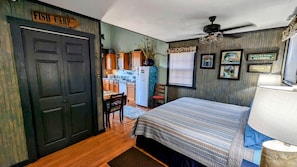 A room with a bed, a desk, a chair, a refrigerator, and a door labeled 'Fish Camp'. - Sparta Serenity: Charming Cabin with Hot Tub and Scenic Farm Views in TN (Sparta)