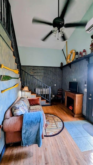 A living room with a sofa, a fireplace, a TV, and a staircase. - Sparta Serenity: Charming Cabin with Hot Tub and Scenic Farm Views in TN (Sparta)