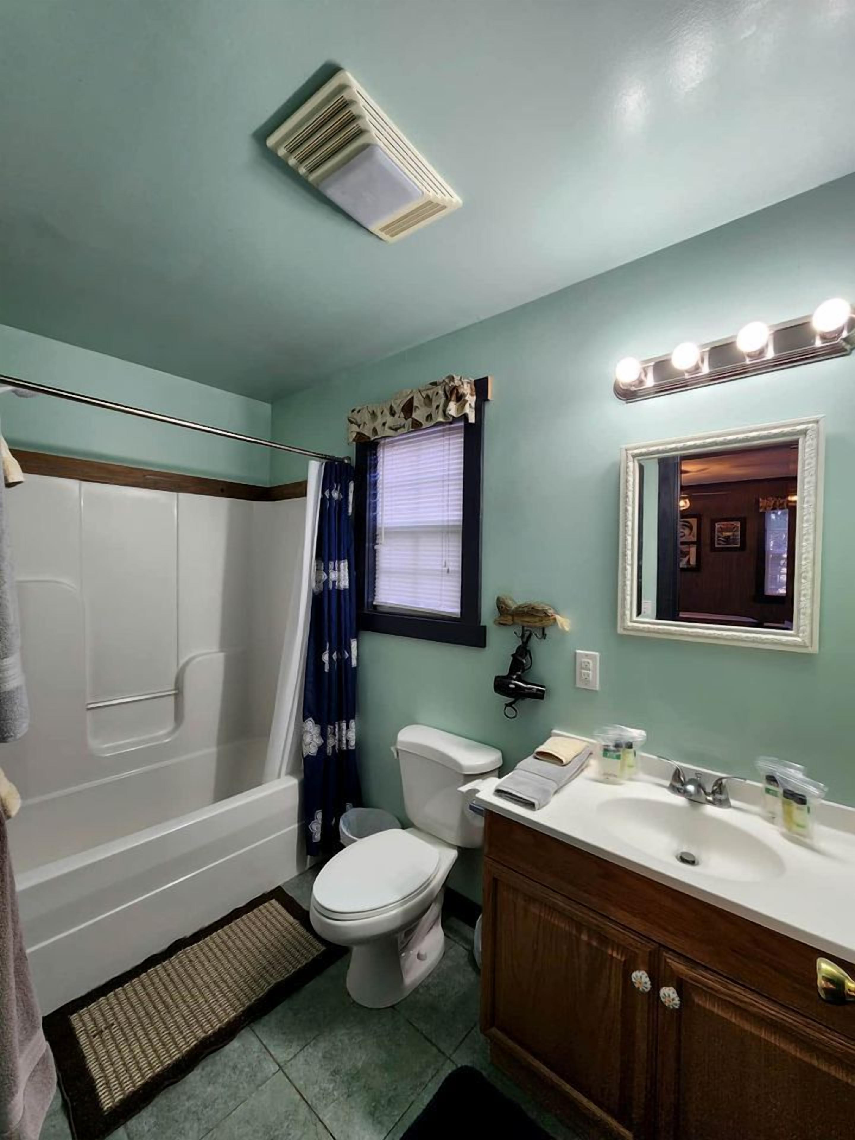 Baño con ducha, inodoro, tocador y espejo con luces.