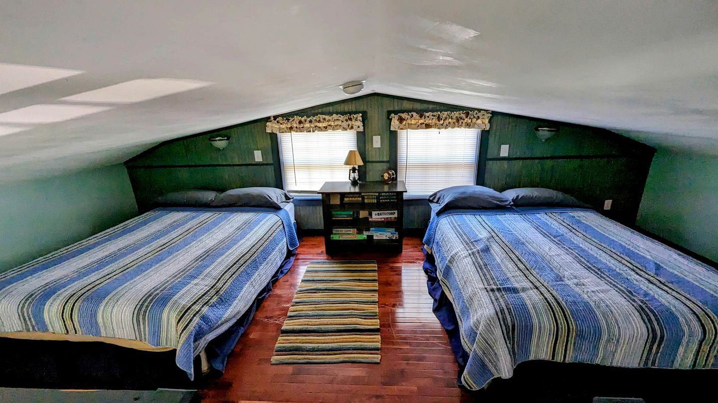 A small attic bedroom with two beds, a wooden floor, and a window with curtains.