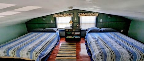 Un dormitorio ático pequeño con dos camas, suelo de madera y una ventana con cortinas.