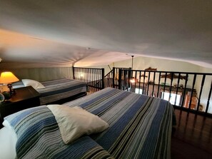 Ein Zimmer mit zwei Betten, einem Nachttisch, einer Lampe und einem Balkon mit Geländer.