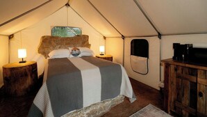 Ett rum med tältliknande inredning, en säng, två sänglampor, ett träskåp och en väggmonterad tv.