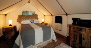 A tented room with a bed, two bedside lamps, a television, and a wooden cabinet.