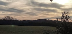 Un paisaje con un campo y árboles a lo lejos bajo un cielo nublado.
