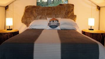 A tented room with a large bed, two bedside lamps, and a pillow with a logo.