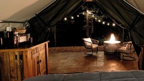 Ein Zelt mit Feuer, zwei Korbstühle und einem Holzschrank.