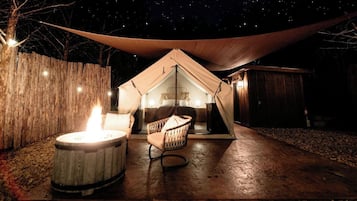 A tent with a fire pit and a chair, set against a night sky.