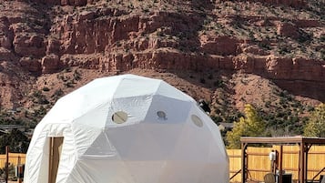 Una tienda en forma de domo geodésico con puerta y ventanas, con montañas al fondo.
