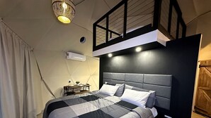 Un dormitori modern amb llit, taules de nit i una làmpada penjant.
