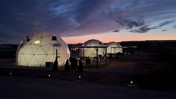 Estruturas em cúpula geodésica com assentos e mesas, ao pôr do sol.
