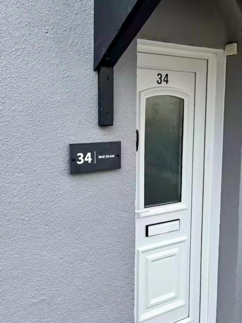 Een witte deur met het nummer 34 en een zwart bordje waarop het adres 34 Well Street staat.