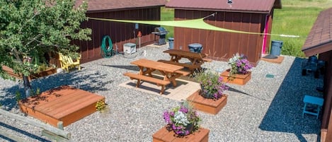 Eine Terrasse mit Holzbänken, Blumenkübeln, einem Grill und einer überdachten Sitzgelegenheit.