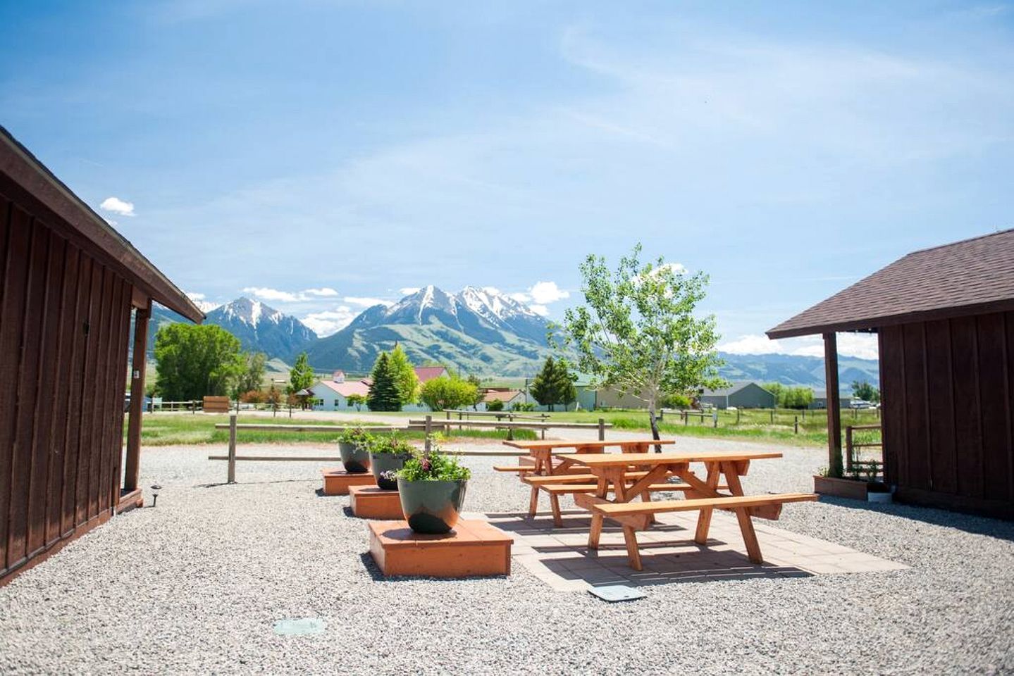 A gravel patio with wooden benches and planters, wooden buildings, and a mountain view.