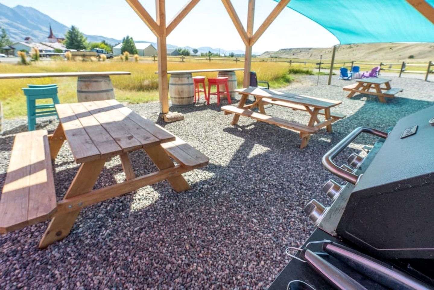 A covered outdoor area with picnic tables, a barbecue grill, and a gravel ground.