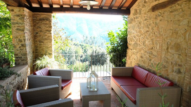A covered patio with wicker furniture and a red cushioned sofa. - "Casa il Noce" in the hills of Lucca with swimming pool 30 min from the sea of Viareggio (Pescaglia)
