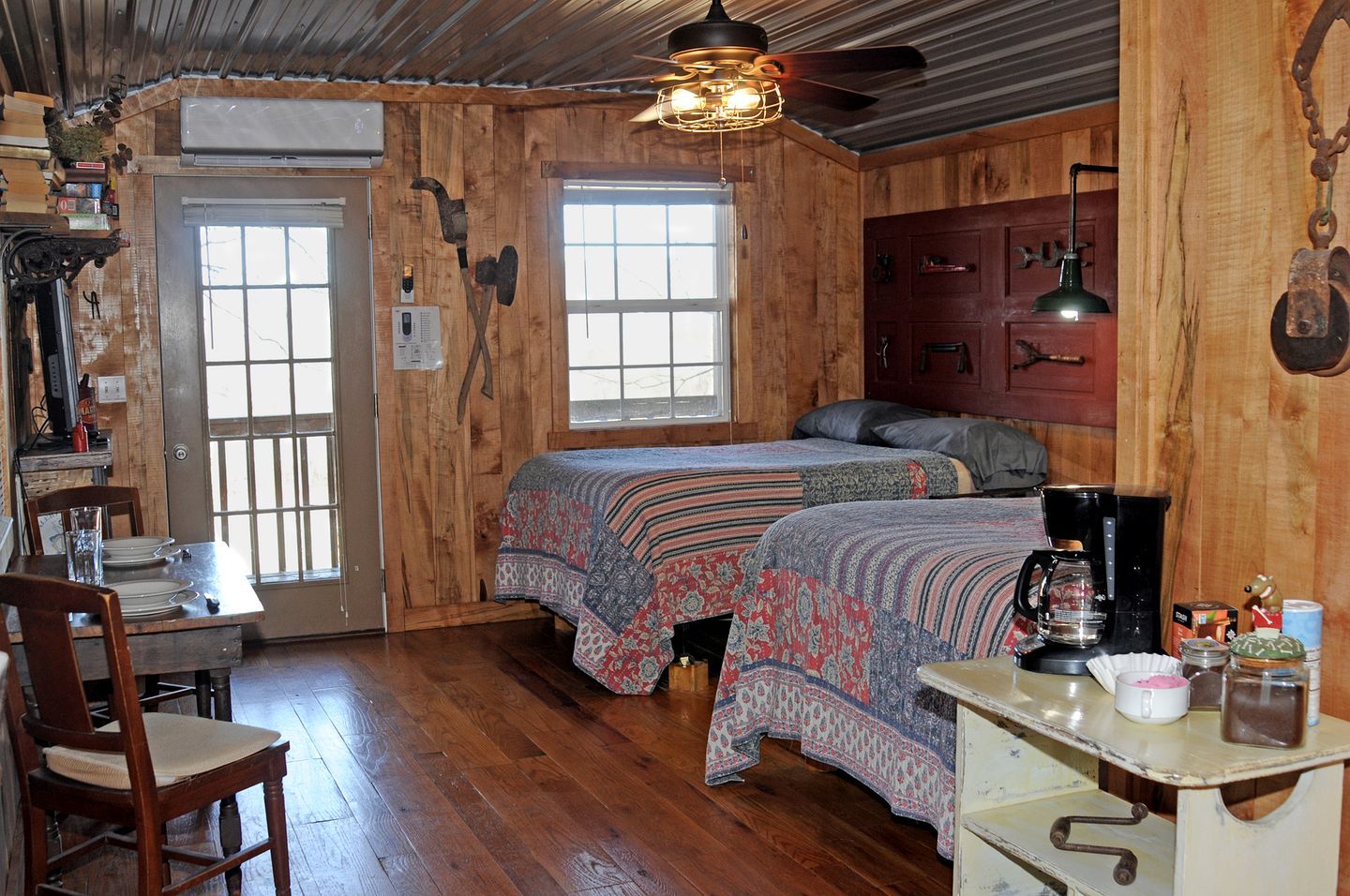 A rustic cabin-style room with two beds, a dining table, and a kitchenette.