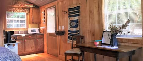 Interior de una cabaña de madera con cocina, comedor y una ventana con persianas.