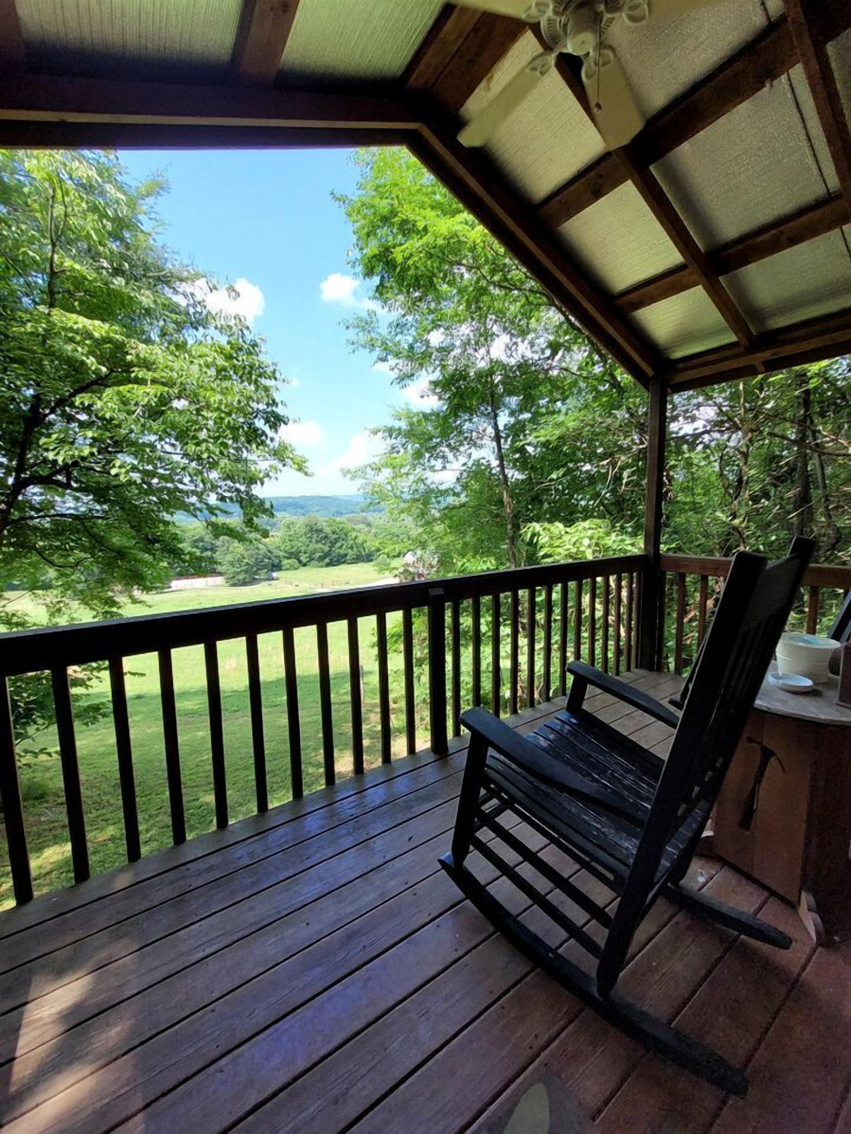 A wooden deck with a bench, a railing, and a view of a green landscape.