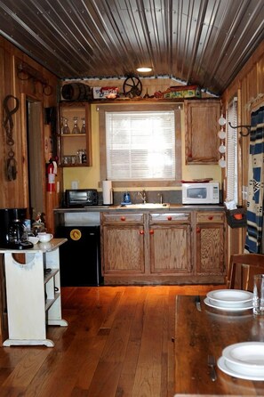 A compact kitchen with wooden cabinets, a microwave, a sink, and a dining table set for two. - Sparta's Hidden Gem: Unique Views Cabin for an Intimate Escape (Sparta)