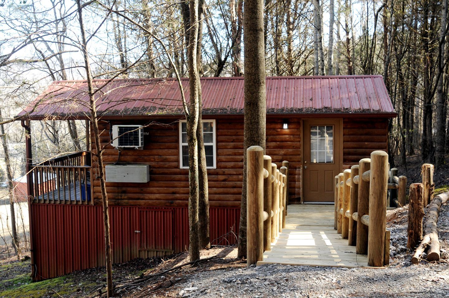 A log cabin with a metal roof, a wooden porch, and a gravel path leading to the door.