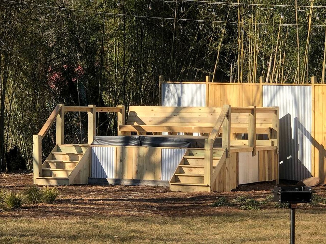 Une structure en bois avec un escalier menant à une plateforme, le tout entouré d’une clôture métallique et d’arbres.