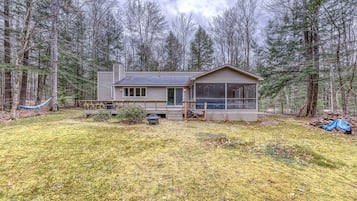 A cabin with a deck, surrounded by a forest.